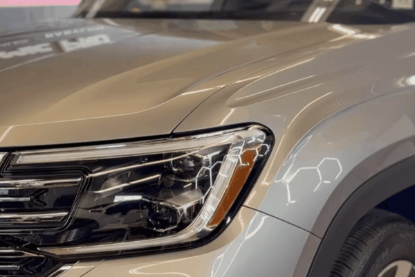 Close-up of a silver SUV's glossy hood, headlight, and fender showing the exterior paint finish